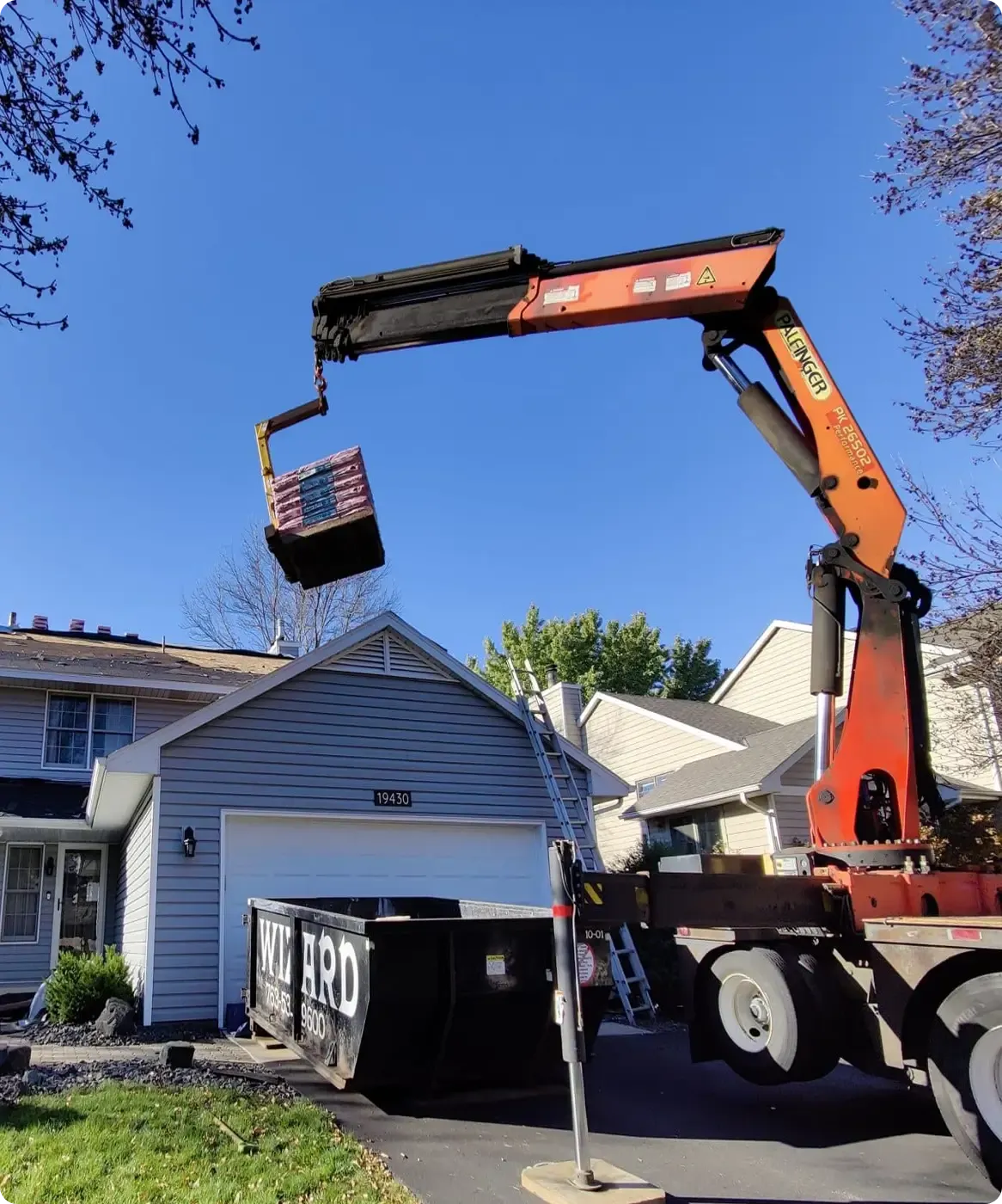 A crane lifts materials in front of a gray house.