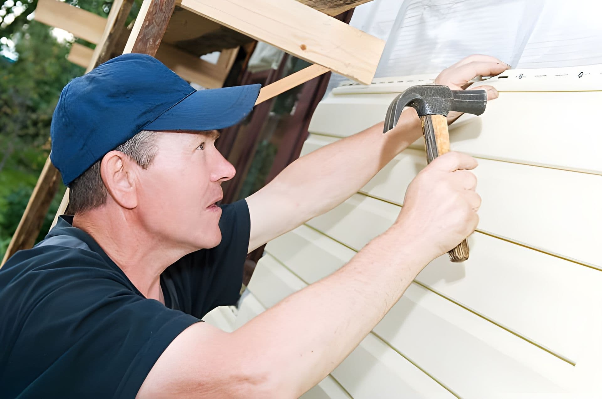 A worker installs new light-colored siding.