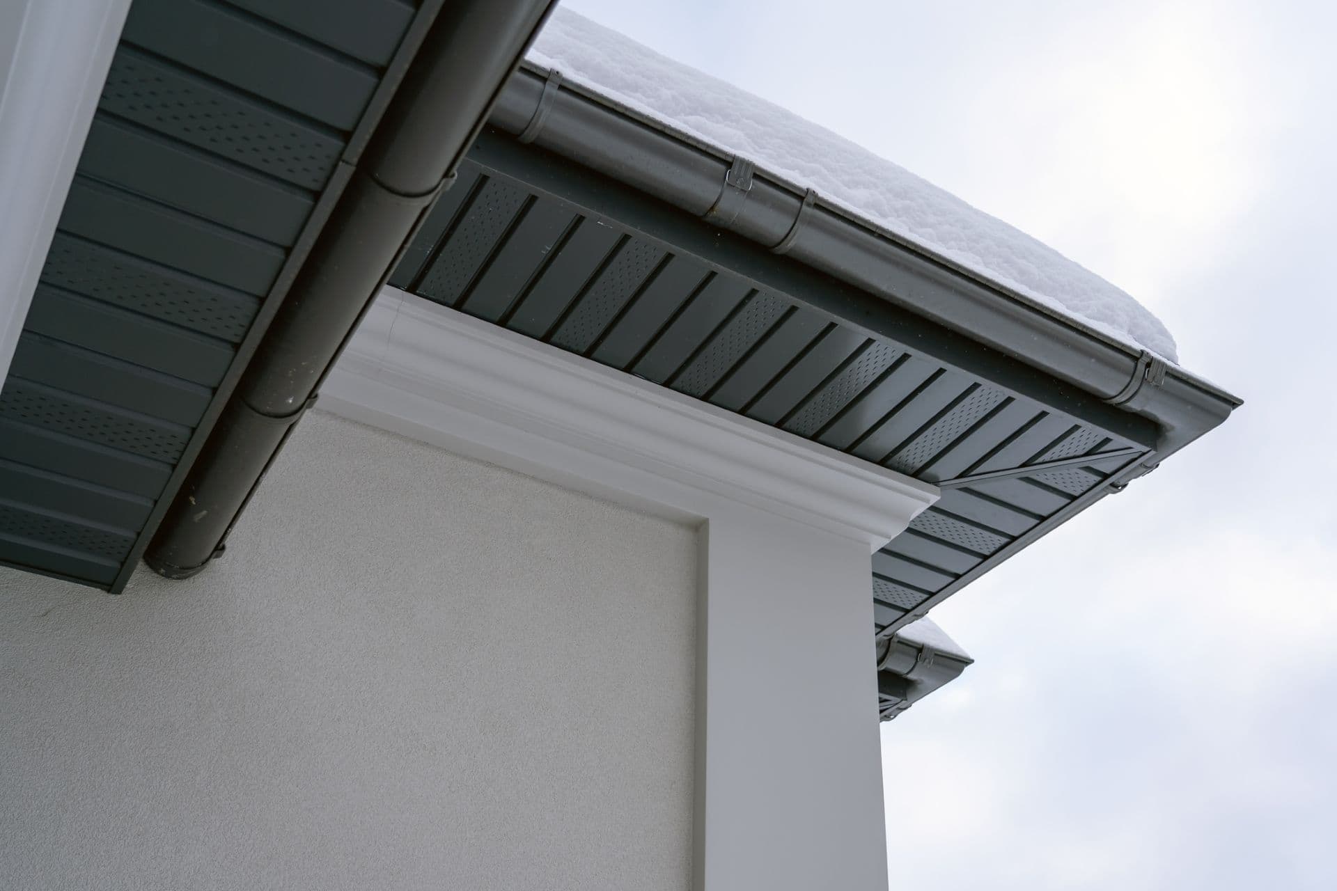 A white house in the winter with dark gray fascia.