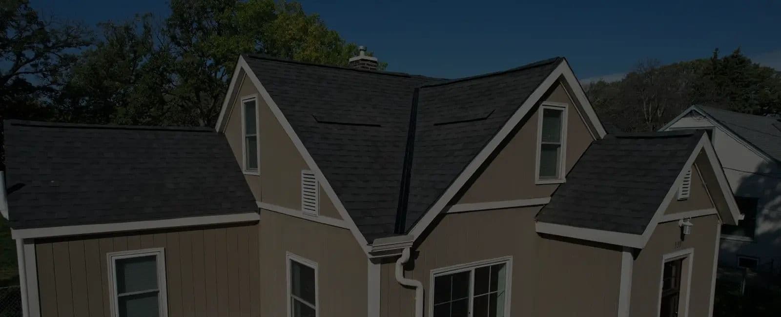 A tan house with new gray shingle roofing.