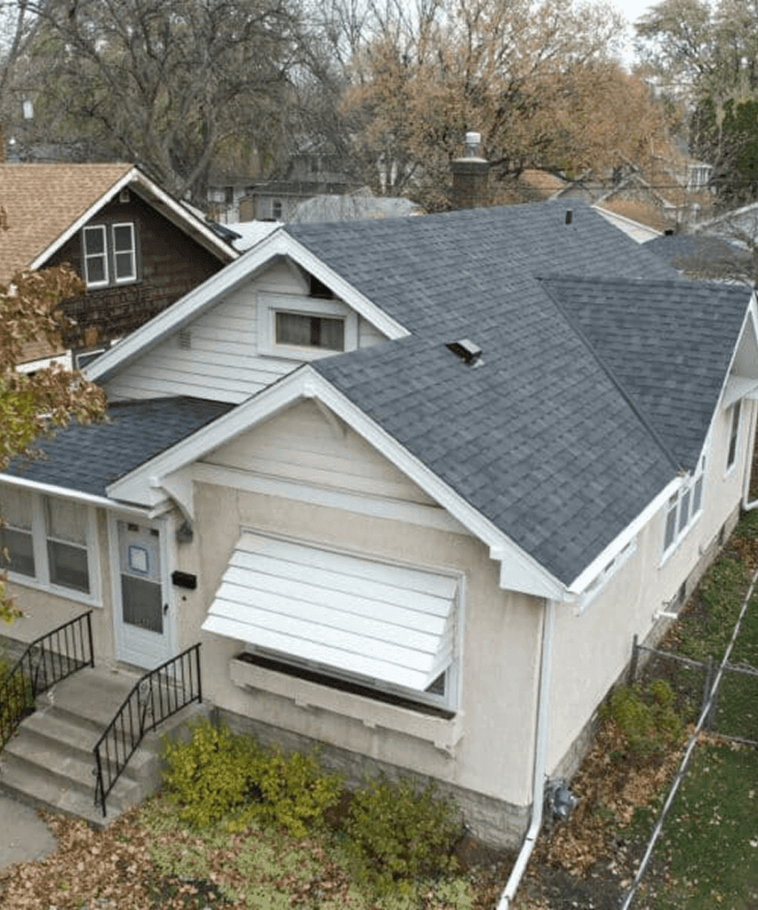 A white and tan house with a new gray shingle roof and a window with a white metal awning.