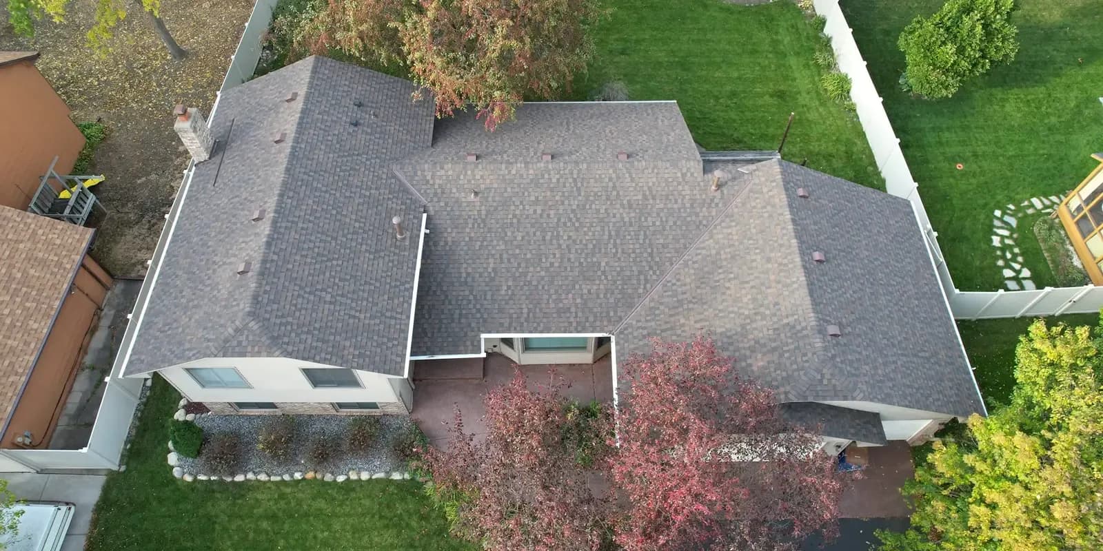 An aerial view of a house with new gray shingle roofing and paved patio.