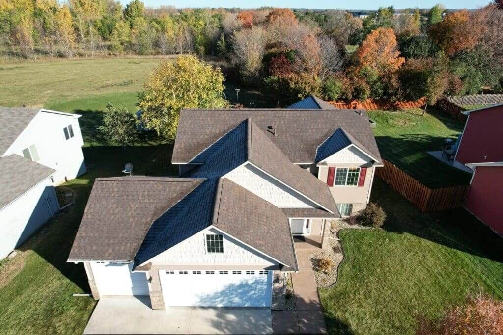 An aerial view of a white and tan house with a new shingle roof during the autumn.