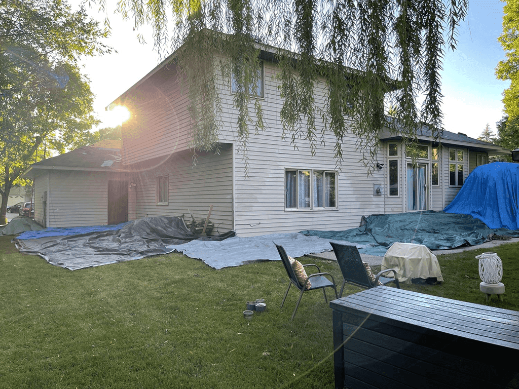A white house in the process of roof replacement with tarps surrounding it.