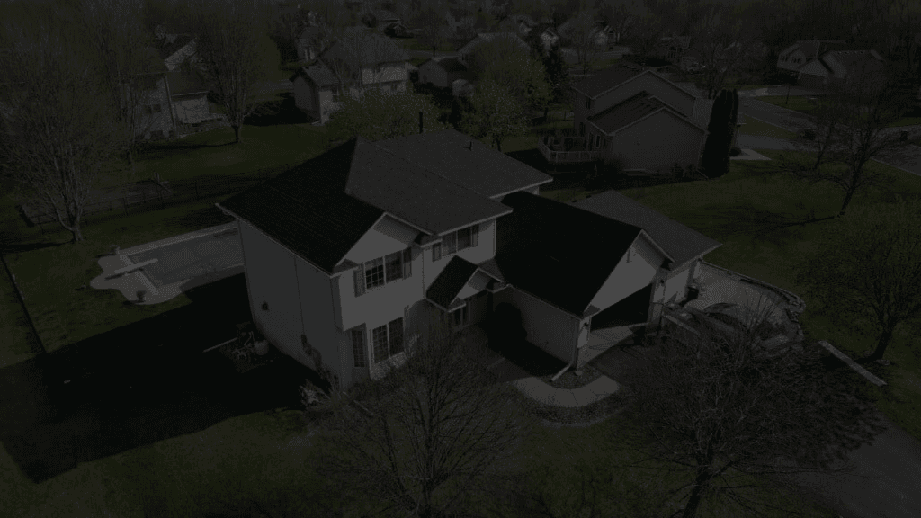 An aerial view of a white house with red shutters and new dark gray shingle roof.