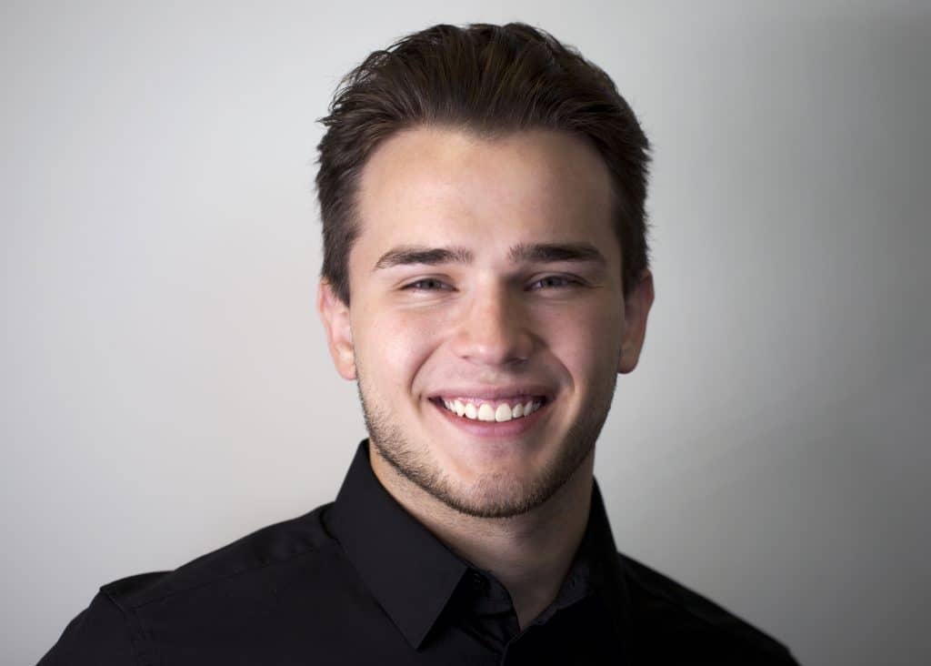 Portrait of a young man with short hair, smiling, and wearing a black shirt.