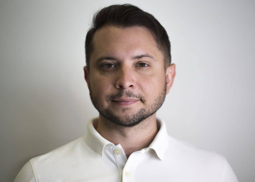 Portrait of a man with short hair and a beard, wearing a white polo shirt.