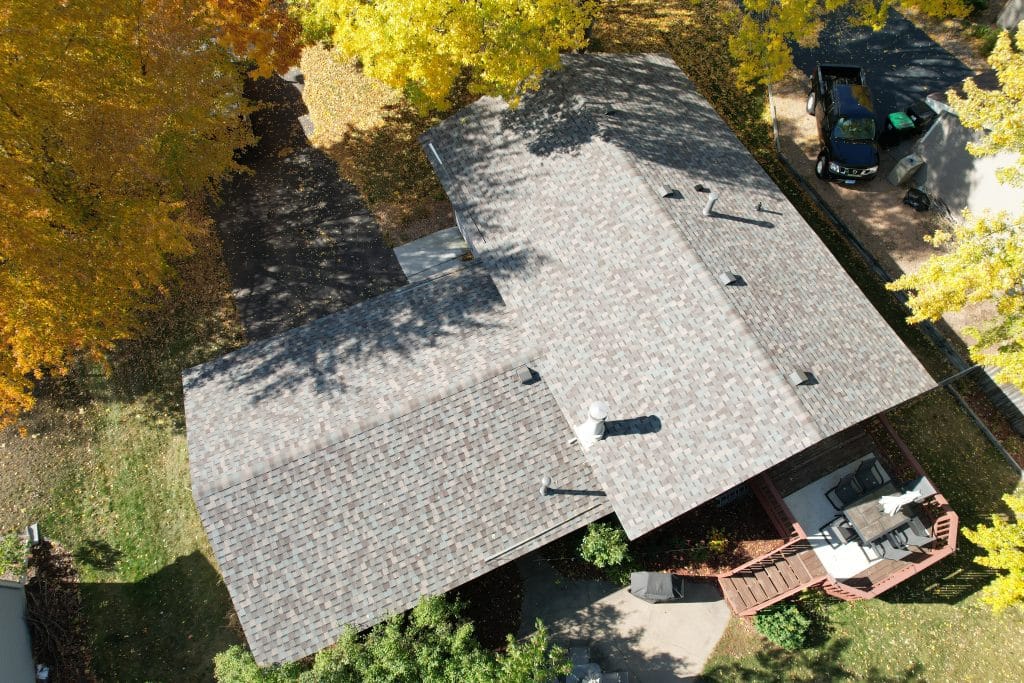 Arial view of a house with a freshly installed roof, set amid autumn trees with golden foliage, showcasing a backyard deck with outdoor furniture.