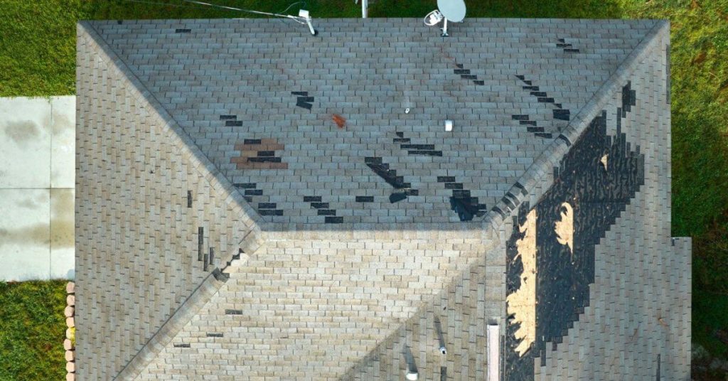 Wind damaged house roof with missing asphalt shingles after hurricane