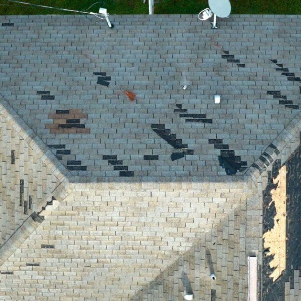 Wind damaged house roof with missing asphalt shingles after hurricane